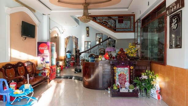 Un vestíbulo de hotel con mostrador de recepción, una escalera y un área de descanso con sillas.