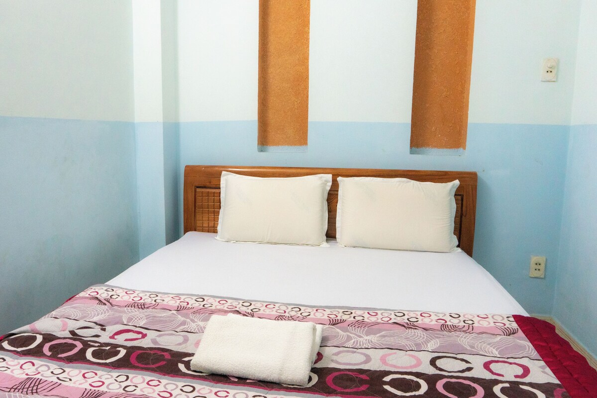 A single bed with a wooden headboard, two pillows, and a patterned bedspread.