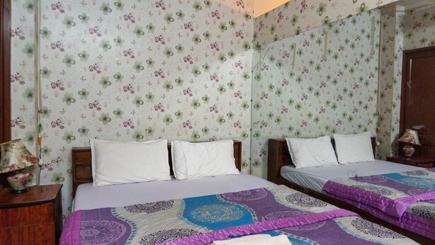 A room with two beds, floral wallpaper, and a mirror on one wall. - Khanh Vy Hotel Binh Tan (Ho Chi Minh City)