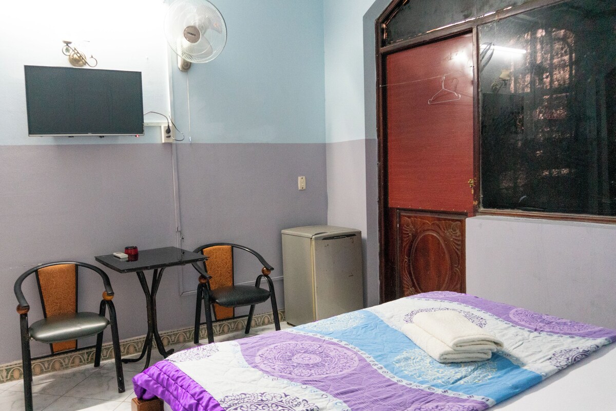 Una stanza con un letto, due poltrone, una scrivania, una televisione e una ventola.