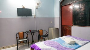 Une pièce comprenant un lit, deux chaises, une table, un téléviseur et un ventilateur.