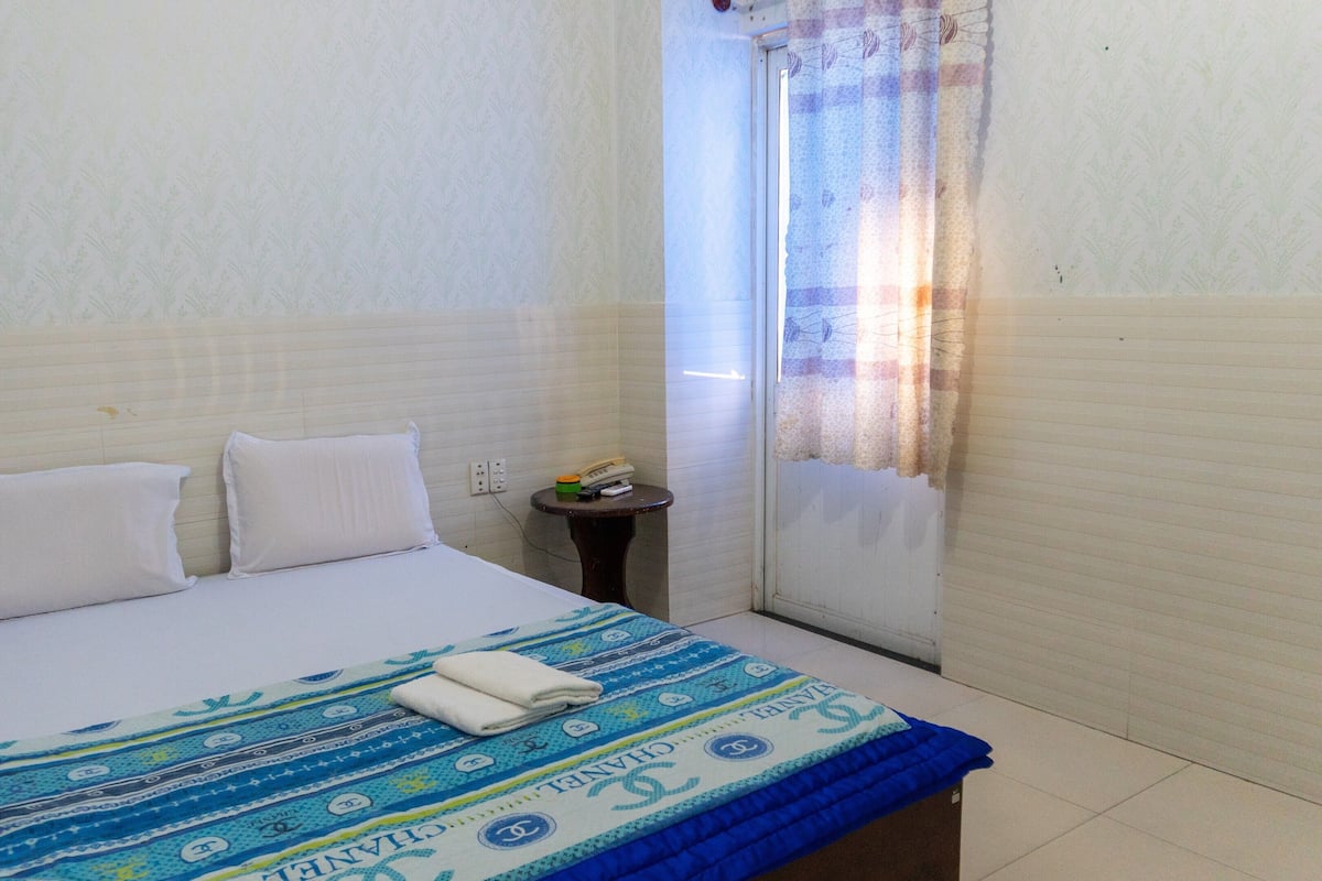A small, clean room with a bed, a bedside table, and a window with curtains.