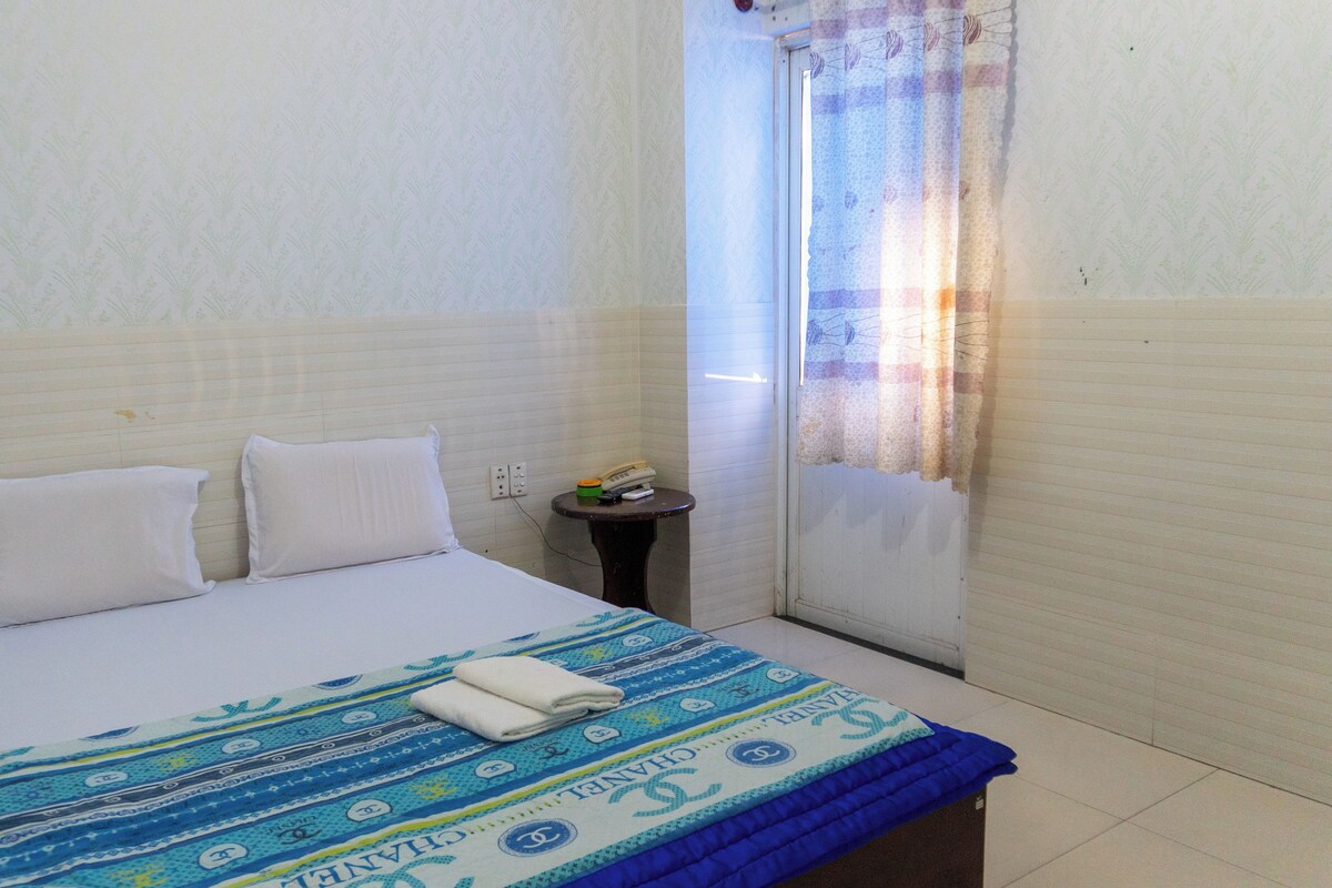 A small, clean room with a bed, a small table, and a window with curtains.