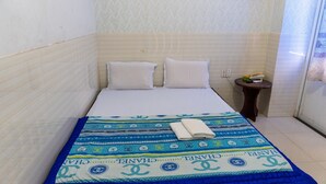 Een klein, netjes opgemaakt bed met een blauw-witte deken met Chanel branding, een nachtkastje met een telefoon en een klein vaasje, en een bloemen behang.