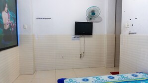 Een hotelkamer met een betegelde vloer, een flatscreen televisie aan de muur, een ventilator en een bed met een Chanel deken.