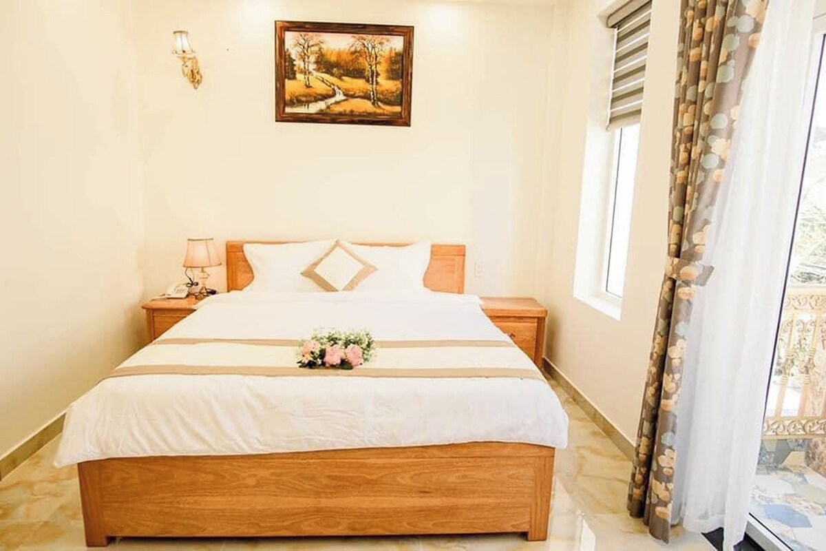 Un letto rifatto con cura, un comodino con una lampada e un bouquet di fiori sul letto.