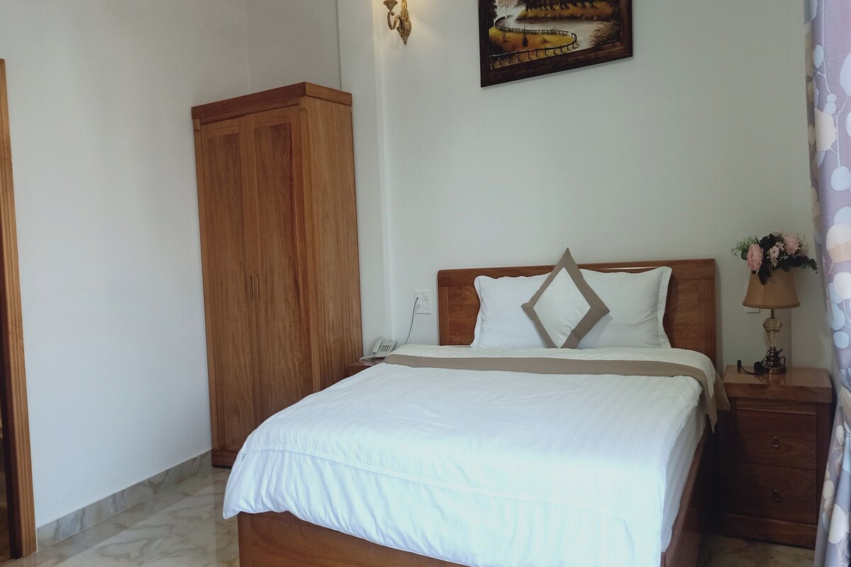 Una cama bien tendida con cabecera de madera, una mesita de noche con lámpara y un armario en una habitación de hotel.