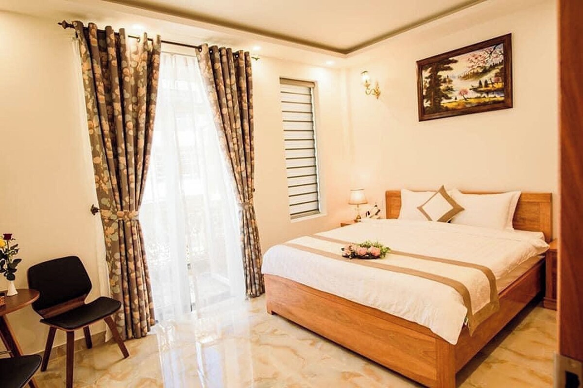 A hotel room with a bed, a chair, a desk, and a painting on the wall.