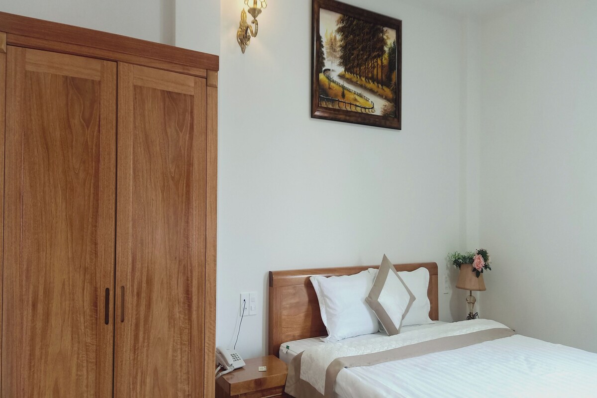 Un dormitorio con un armario de madera, una cama con ropa blanca, una mesita de noche con un teléfono y un cuadro en la pared.