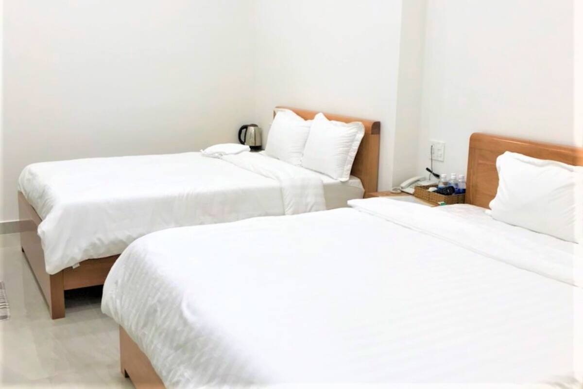 Two single beds with wooden headboards, white bedding, a bedside table with a lamp, and a small table with a kettle and cups.