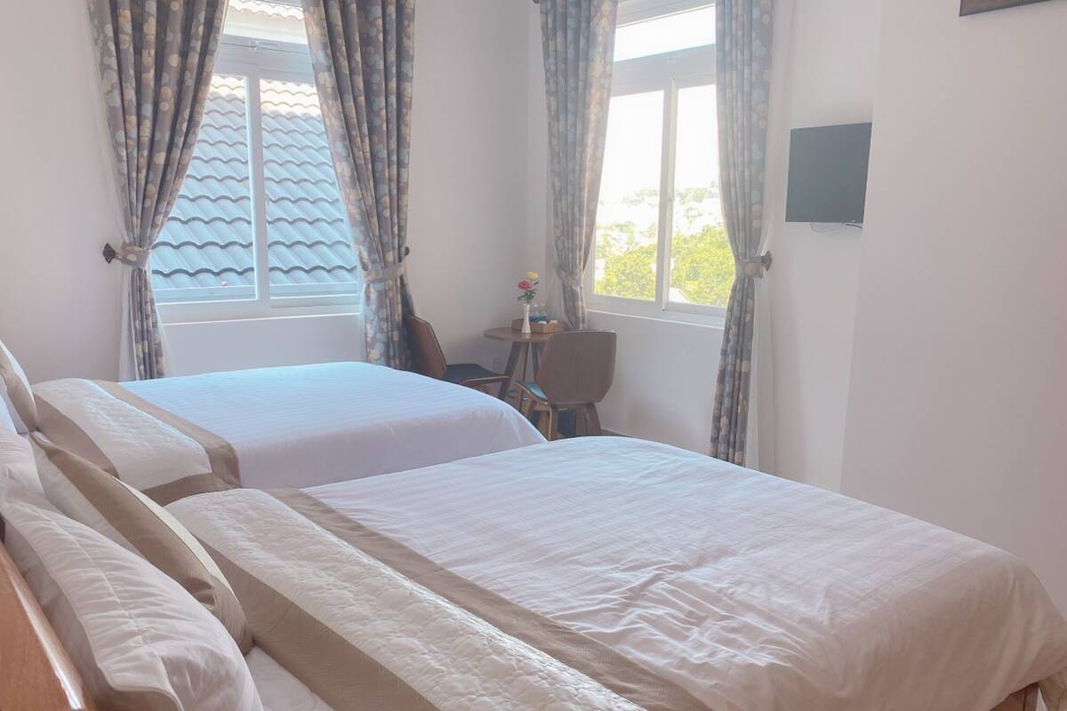 A hotel room with two beds, a small table with a vase, and a TV on the wall.