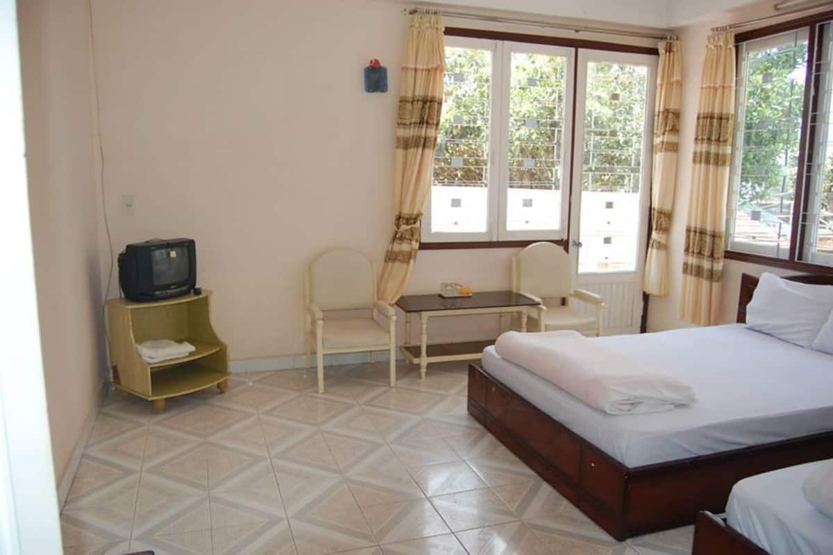 A hotel room with a bed, a small table, a chair, a television, and a window with curtains.