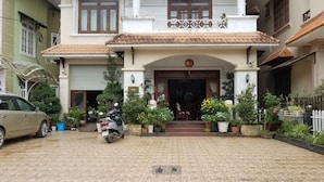 A two-story house with a tiled roof, a front entrance with a decorative arch, and a small porch with potted plants. - Nhat Huy Hotel (Xuan Huong - Da Lat)