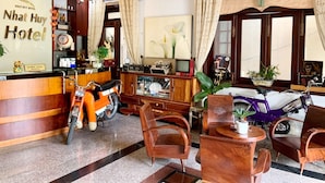 A reception area with a wooden reception desk, a motorcycle, a purple scooter, and a reception counter with a sign reading "Nhat Huy Hotel". - Nhat Huy Hotel (Xuan Huong - Da Lat)