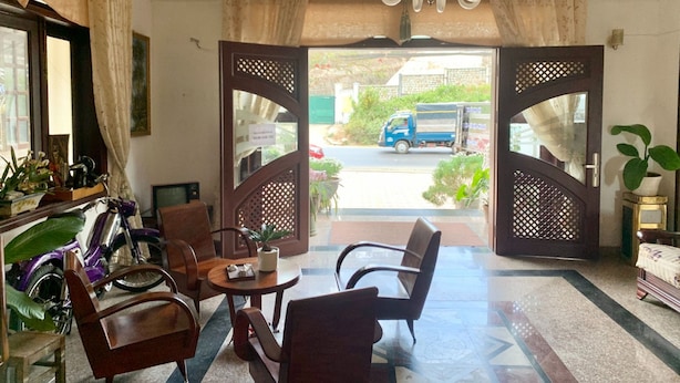 A hotel lobby with a reception desk, seating area, and a view of the street outside. - Nhat Huy Hotel (Xuan Huong - Da Lat)