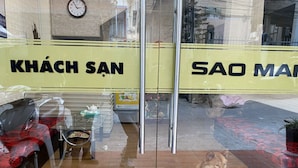 A hotel entrance with a glass door, a clock on the wall, and two dogs sitting inside. - Sao Mai Tim Hotel (Xuan Huong - Da Lat)