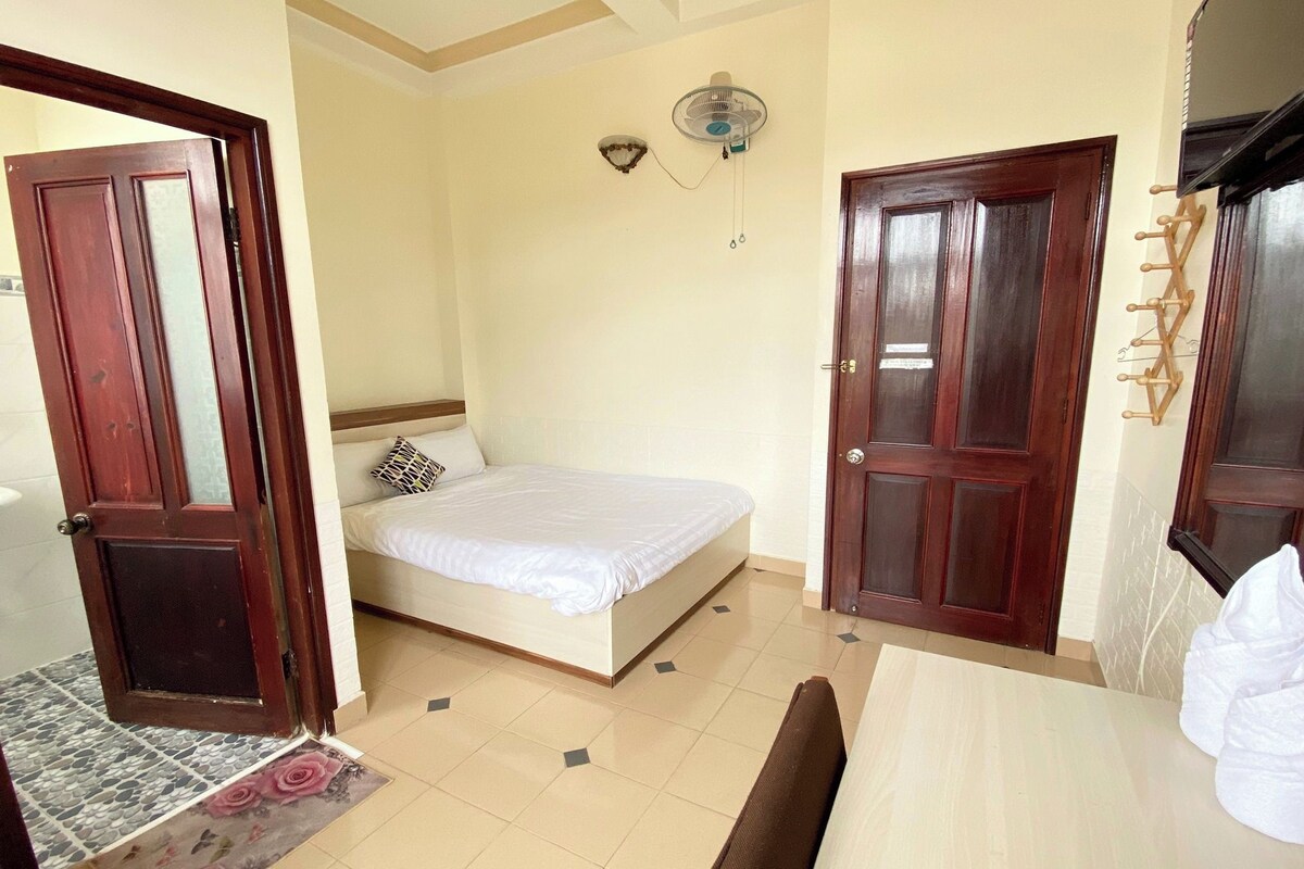 A bedroom with a bed, a wooden door, a fan, and a wall-mounted hook.