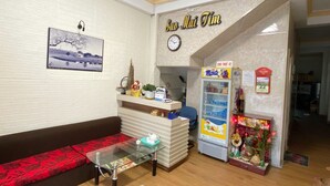 A reception area with a sofa, a glass table, a clock, a refrigerator, and a wall with a framed picture. - Sao Mai Tim Hotel (Xuan Huong - Da Lat)