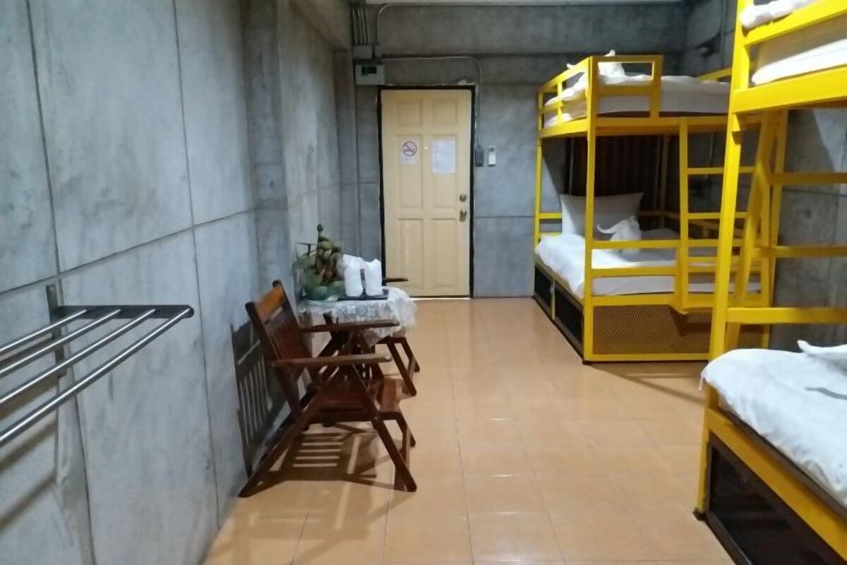 A dormitory room with bunk beds, a wooden chair, a small table, and a radiator.