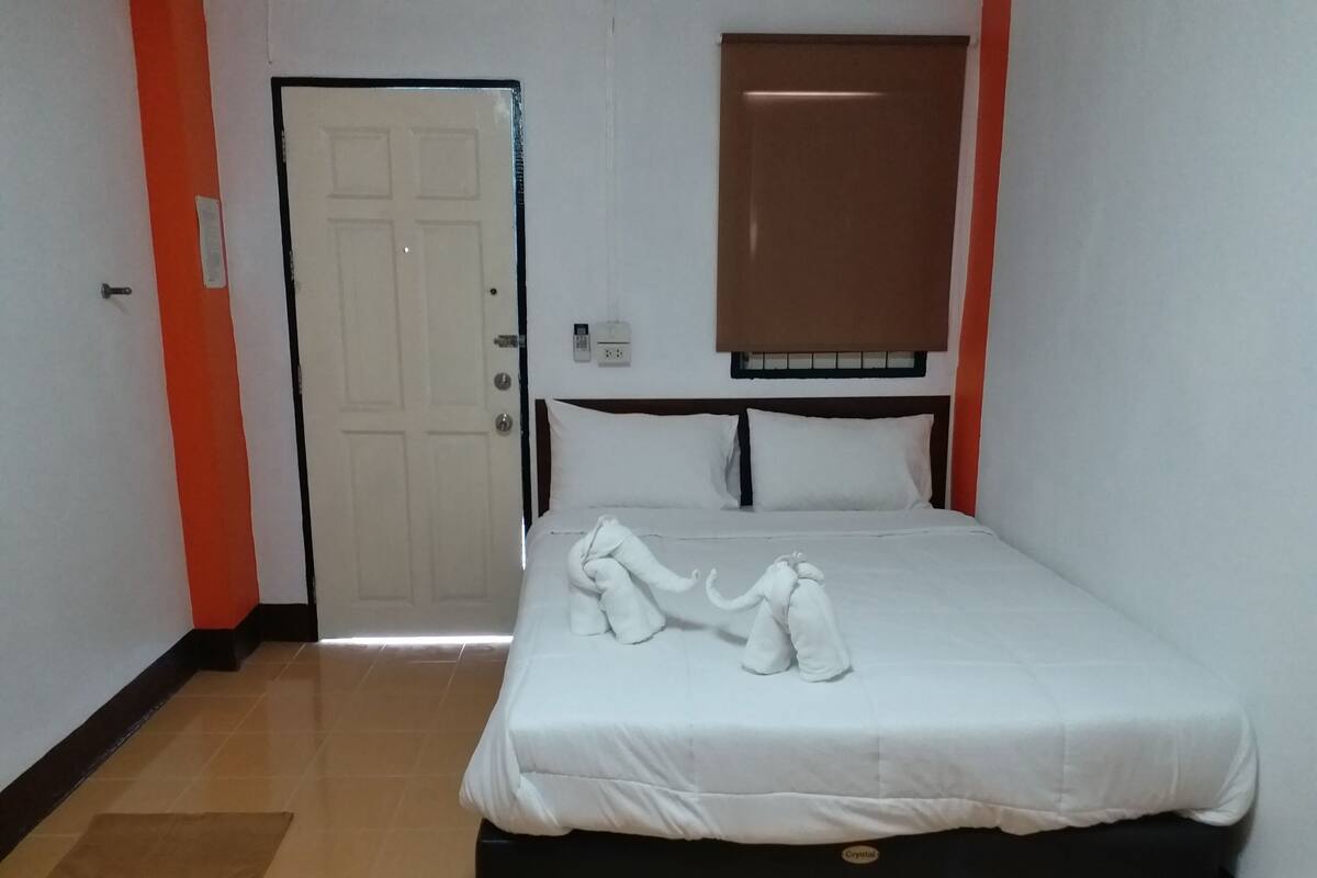 Quarto de hotel com cama, porta, janela e luminária fixada na parede.