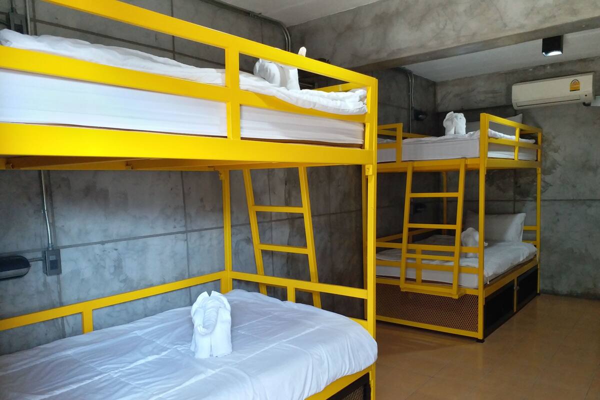 Quarto com beliches, cada um com colchão e travesseiros, e uma escada em uma das camas.