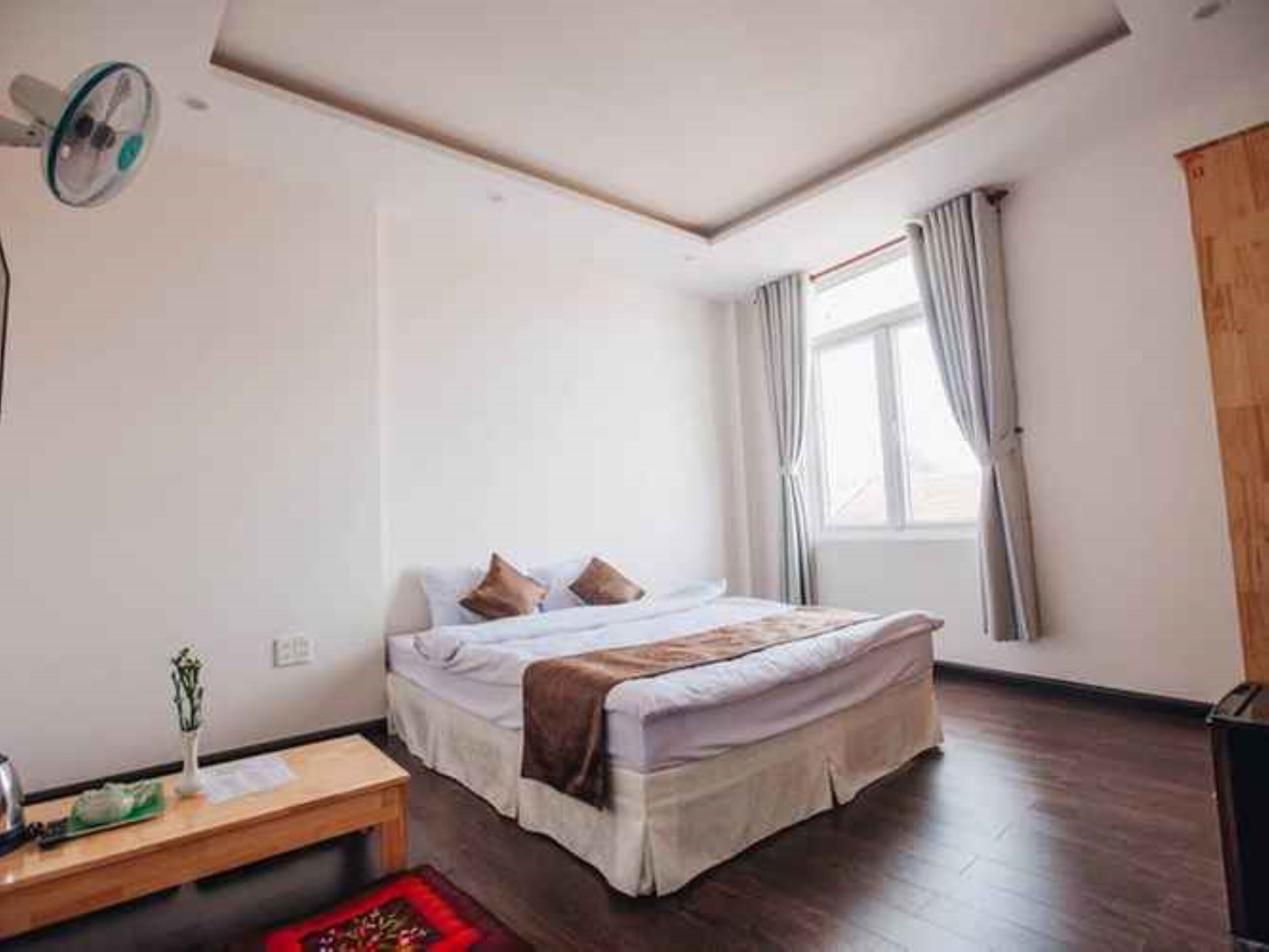 Un dormitorio con cama, mesita de noche, ventana con cortinas y ventilador de techo.