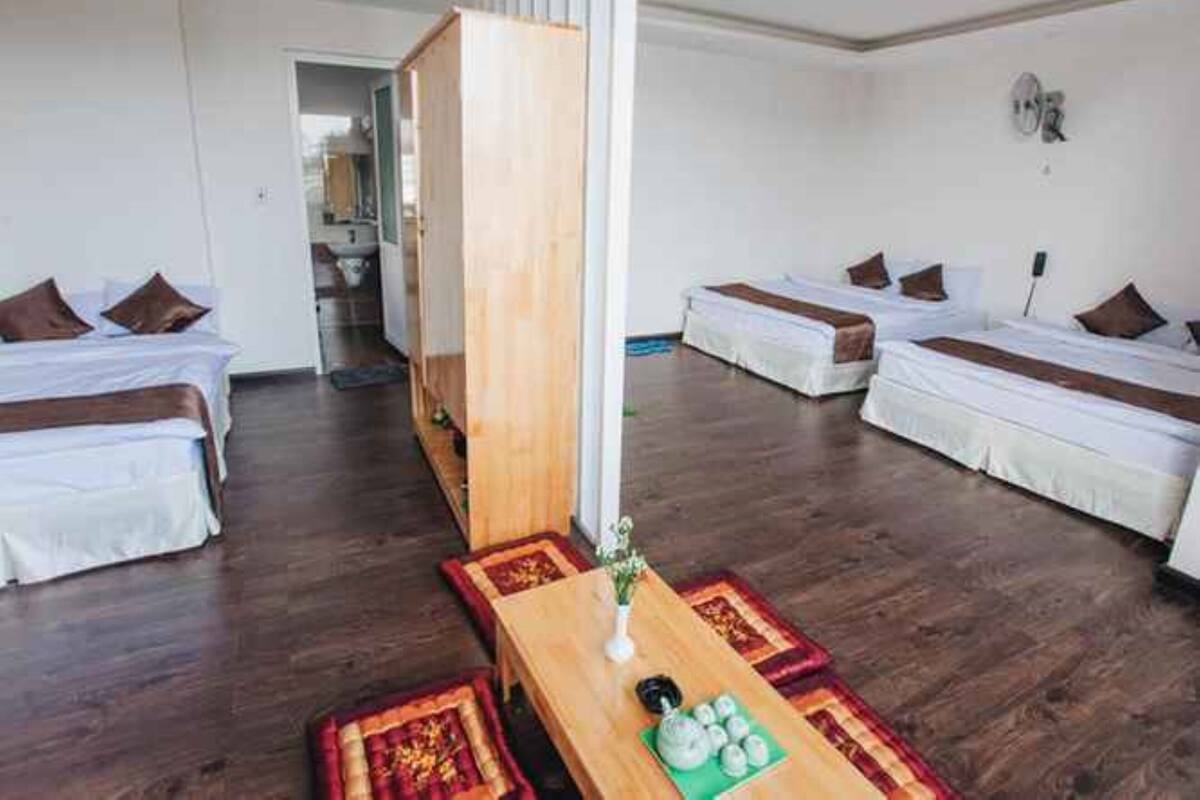 A hotel room with two single beds, a wooden table with a vase and teapot, and a small rug.