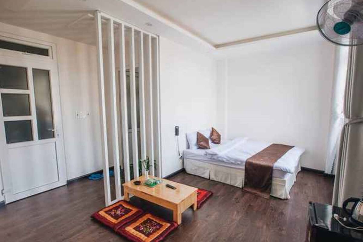 A room with a bed, a wooden table, a fan, and a sliding door.