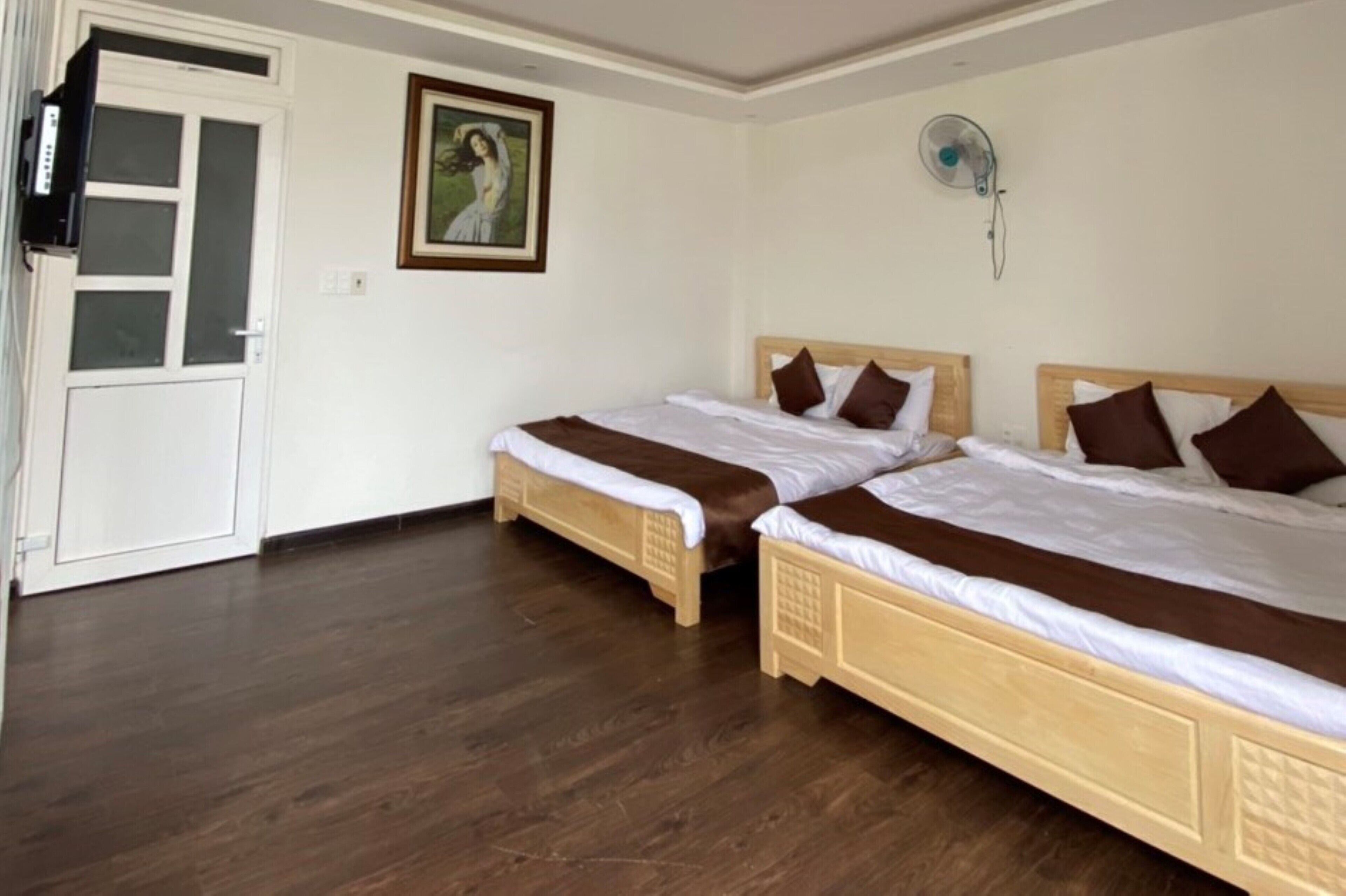 Una habitación con dos camas de madera, una puerta blanca, un cuadro en la pared y un ventilador de techo.