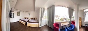 Habitación de hotel con dos camas, un comedor con sillas rojas y azules, y un ventanal con cortinas.