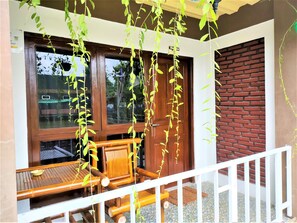 A wooden balcony with a white railing, a wooden table, and chairs. - Bungalow Etnik (Kebumen)