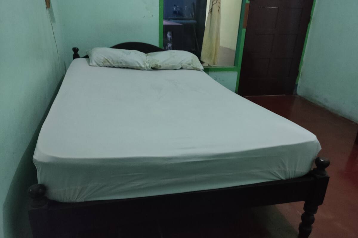 A single bed with a white mattress and wooden frame in a room with green walls and a tiled floor.