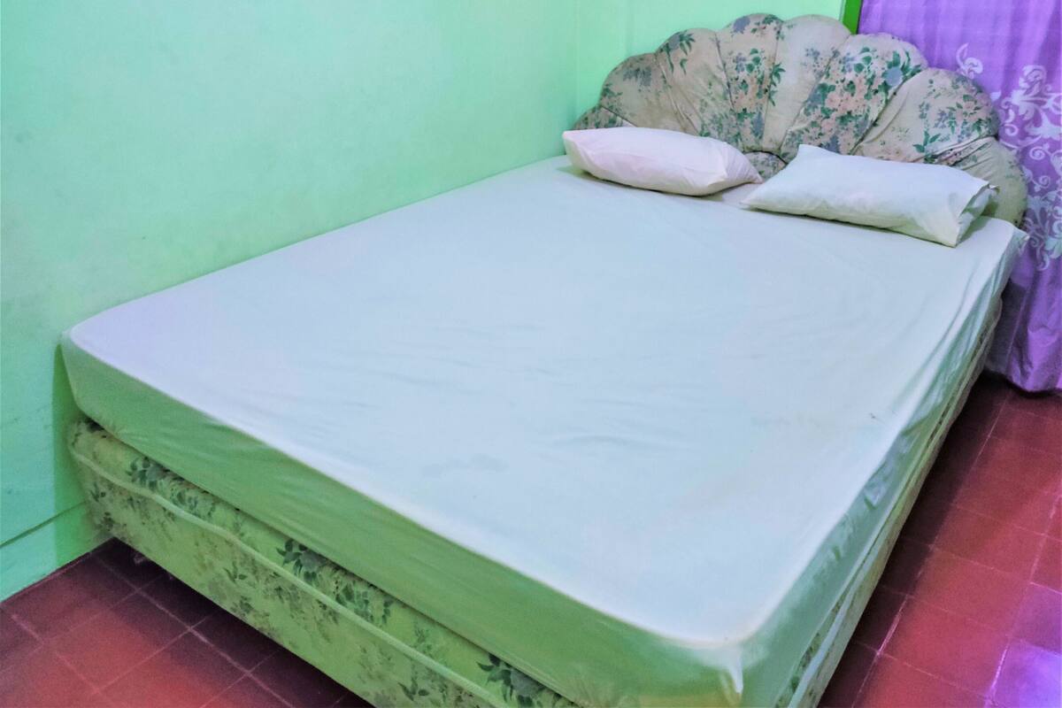 A single bed with a floral-patterned headboard and two pillows, set against a green wall with a purple curtain.