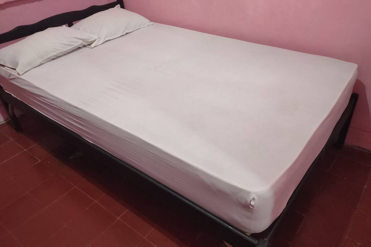 A single bed with a white mattress and pillows, a black headboard, and a red-tiled floor.