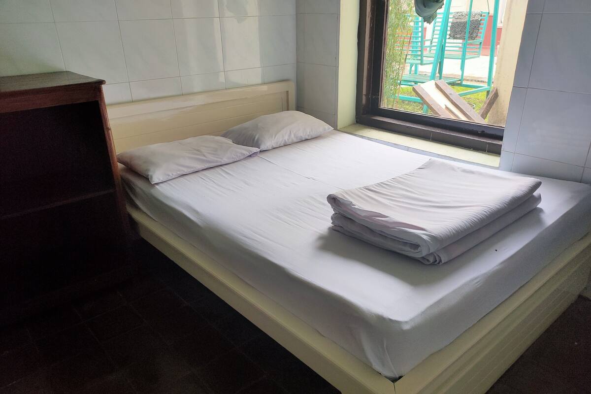 A single bed with white linens, a wooden nightstand, and a window with a view of outdoor furniture.
