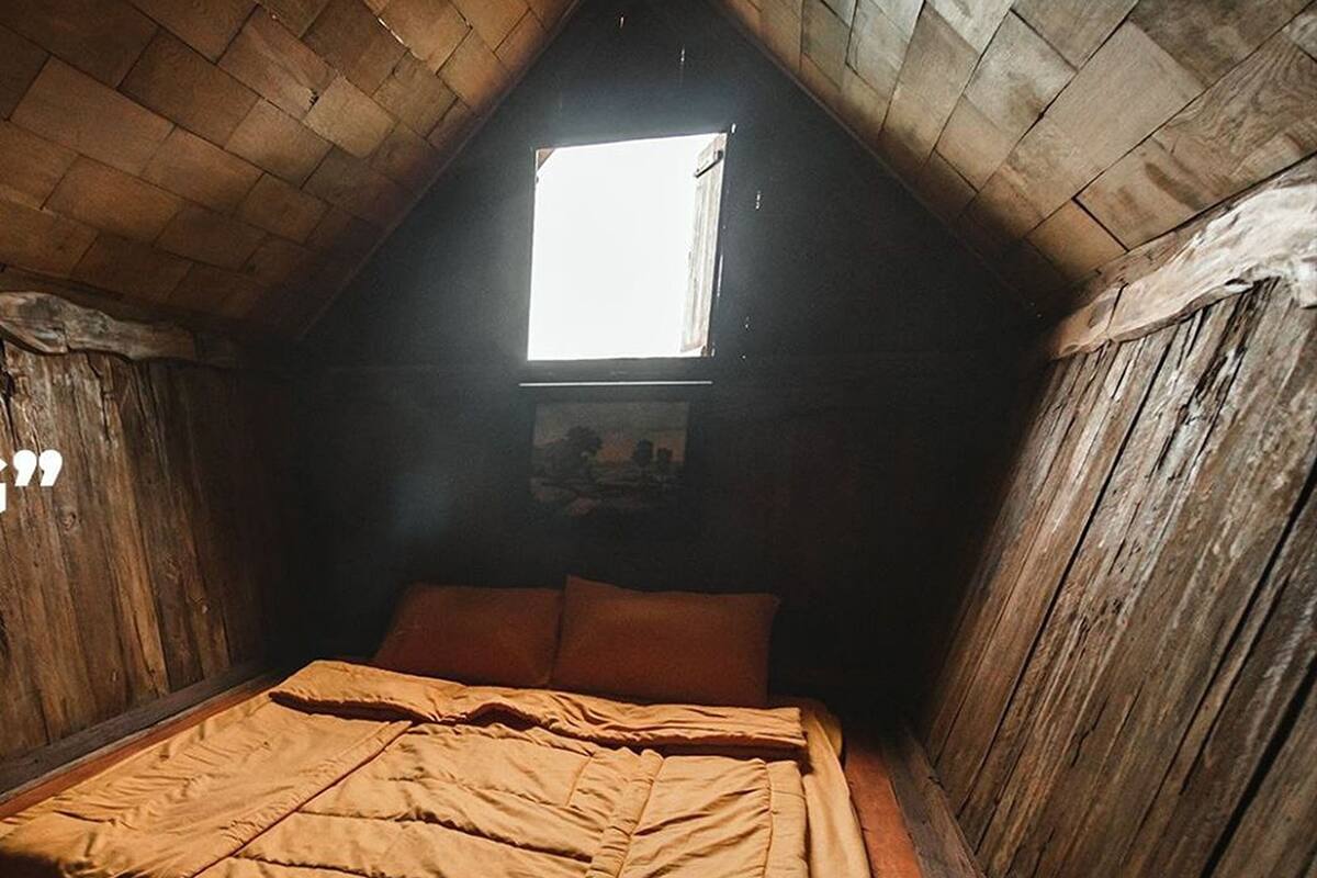 Um quarto de sótão pequeno e acolhedor, com uma cama de solteiro, uma janela e paredes de madeira.