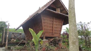Un bâtiment rustique en bois, doté d’un toit en pente, entouré de végétation et d’un tas de briques.