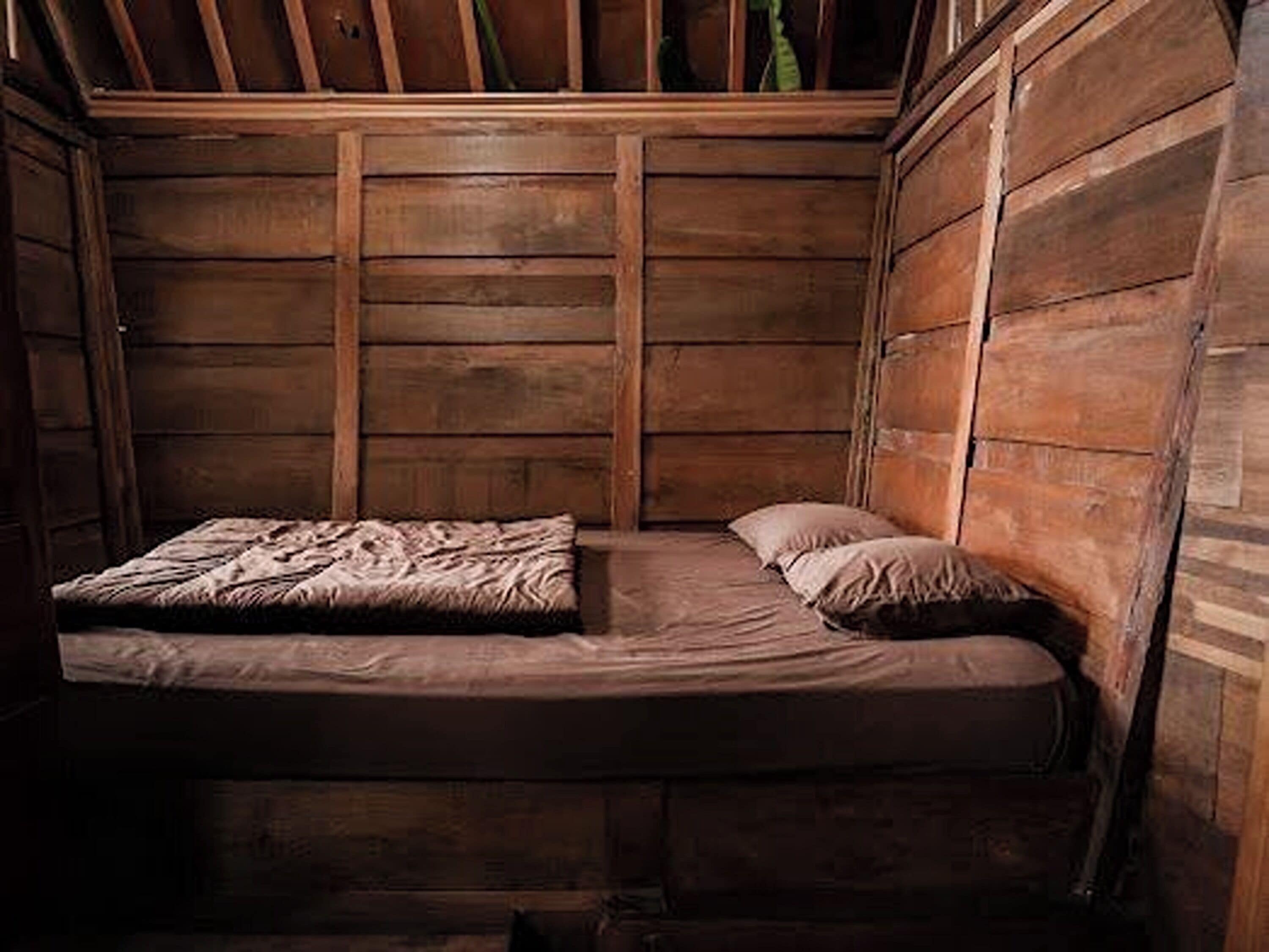 A small, wooden cabin-style room with a single bed and a wooden headboard.