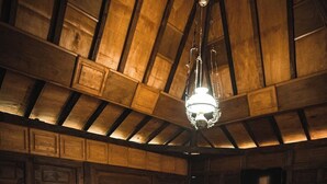 Una habitación de madera con una cama, una mesita y una lámpara colgante.