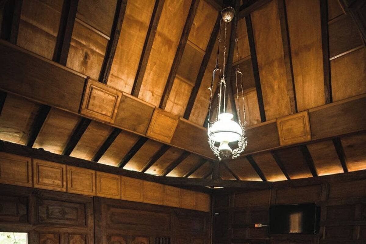 Um quarto de madeira com uma cama, uma mesinha e um lustre.