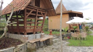 Una estructura de madera con techo de tejas, un banco y un pequeño jardín con sillas y una mesa.
