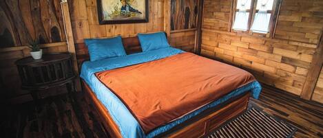 Un dormitorio tipo cabaña de madera con una cama, un cuadro en la pared y una ventana con cortinas.