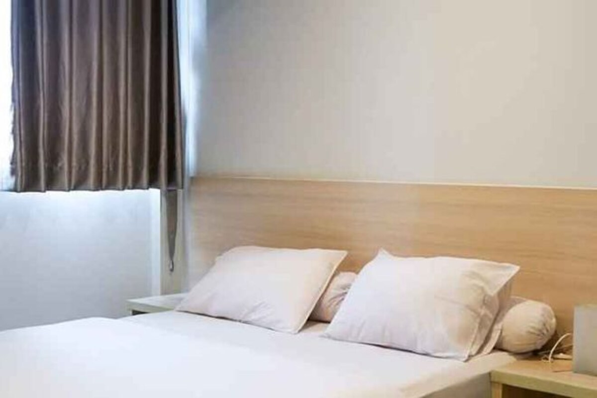 Quarto de hotel com cama, mesa de cabeceira e janela com cortinas.