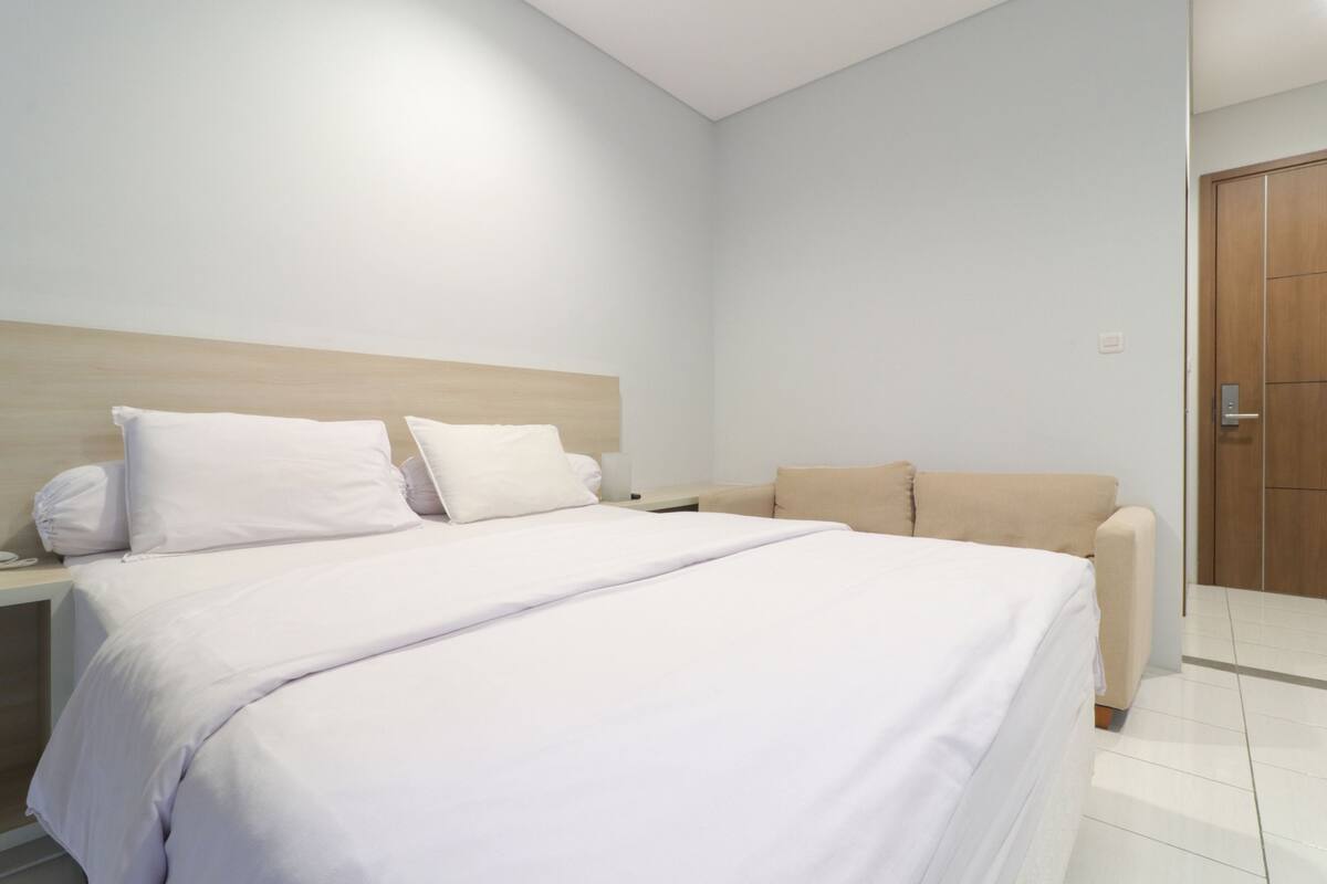 A modern hotel room with a large bed, a bedside table, a nightstand, and a sofa.