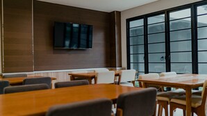 A conference room with a large window, a flat-screen TV mounted on the wall, and several wooden tables and chairs. - Mendjangan Residence (Jakarta)