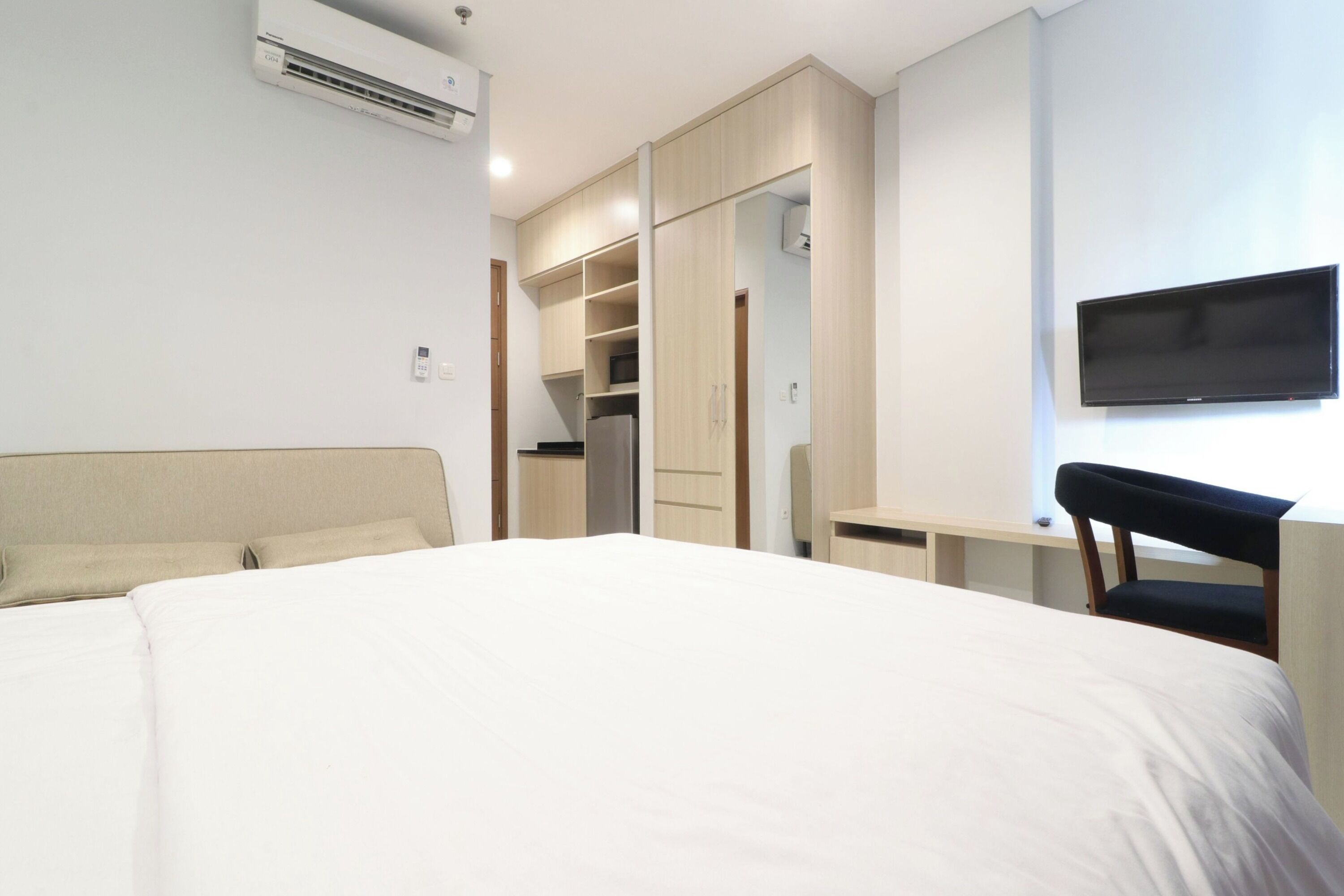 A hotel room with a bed, a desk, a chair, a TV, and a wardrobe.
