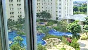 A high-rise building with multiple balconies, a landscaped pool area with various water features, and surrounding greenery. - Apartement Educity Tower Y-P-H By Prafi (Surabaya)