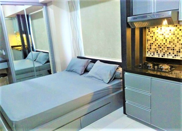 Quarto moderno com cama, mesas de cabeceira, armário embutido e uma kitchenette equipada com fogão e micro-ondas.