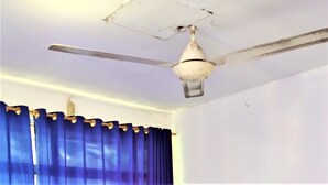 A ceiling fan with a light fixture in a room with blue curtains. - De' Premium Hotel Musi Raya (Palembang)