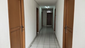 A corridor with tiled flooring, wooden doors, and a ceiling light. - De' Premium Hotel Musi Raya (Palembang)